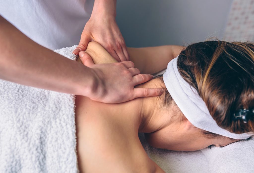 a woman is laying down on a massage table while a person's hands massage the skin on her upper back and shoulders