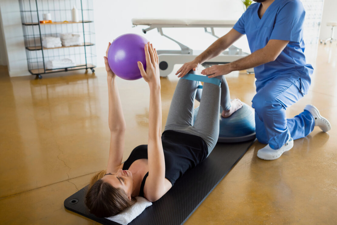 Female patient lying down on a mat, exercising with her physiotherapist 