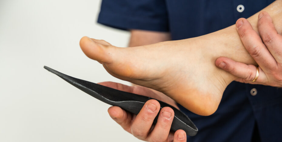 A medical professional is holding someone's foot with one hand and placing a custom orthotic on the sole of the foot using their other hand