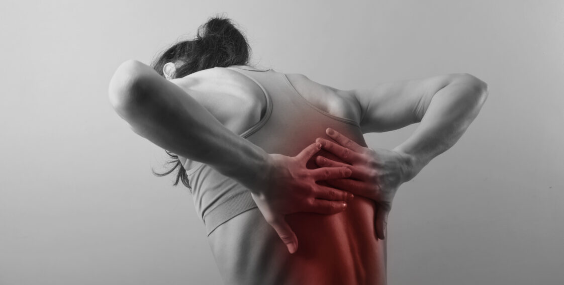 A woman wearing an athletic bra is hunched over. There is a red spot on her back, illustrating pain.