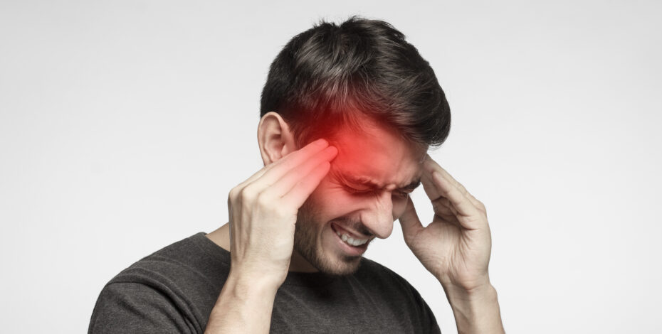 A young man touches his temples. He is wearing a painful expression. There is a red coloration on his forehead, indicating a headache
