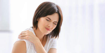 A young woman holds her shoulder and wears an expression of pain