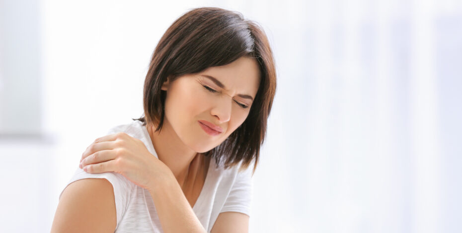 A young woman holds her shoulder and wears an expression of pain